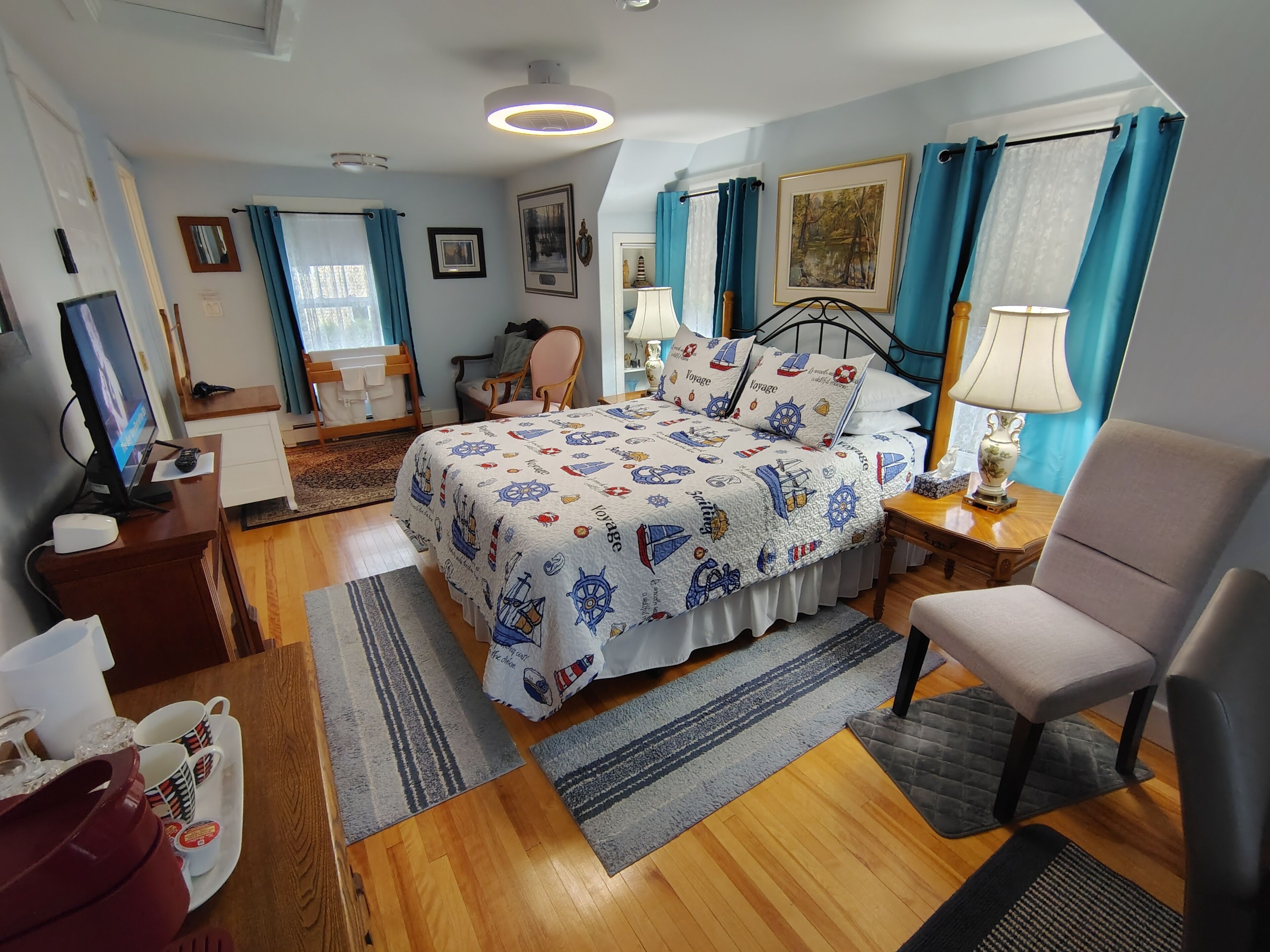 A well-lit bedroom with a bed, a chair, a desk, and a television.