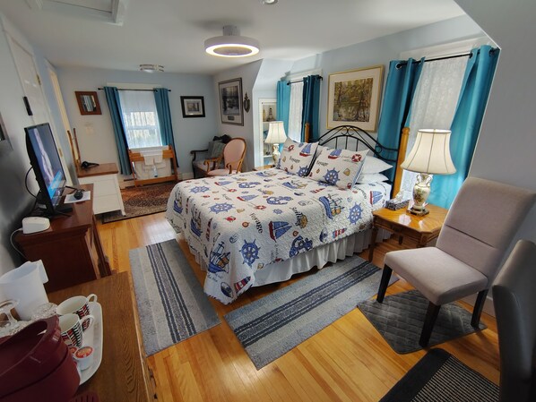 A well-lit bedroom with a bed, a chair, a desk, and a television. - Digby B&B (Digby)