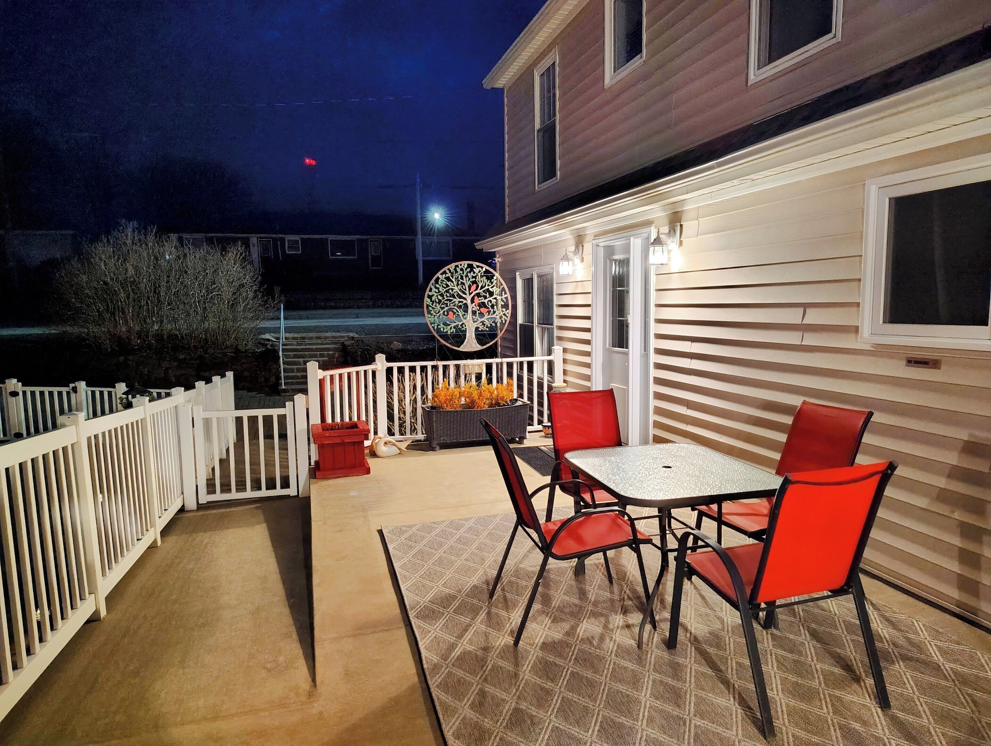 A patio with a table and chairs, a decorative tree sculpture, and a white fence.