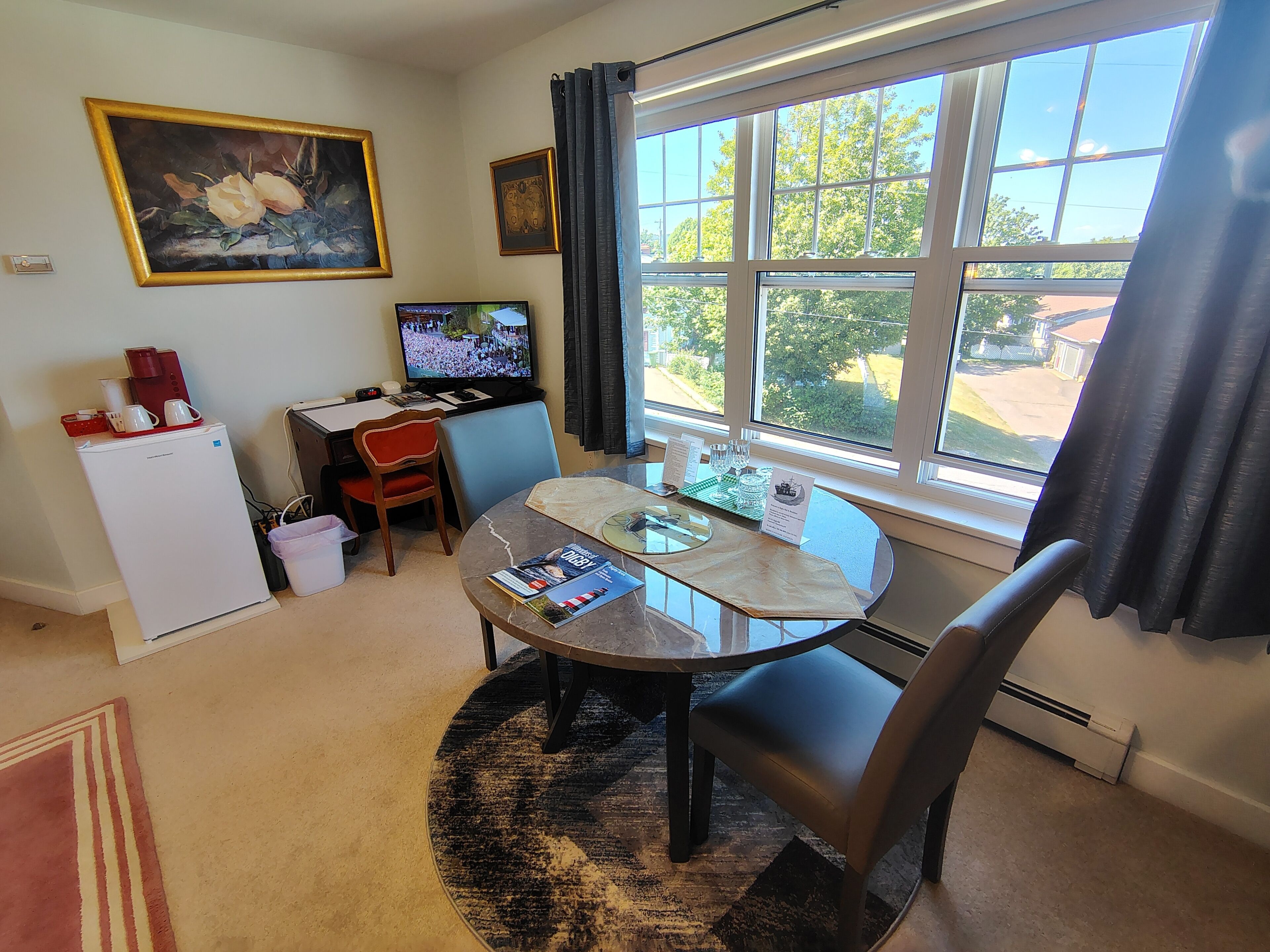 Un espacio habitable compacto con una mesa de comedor, sillas, un refrigerador pequeño, un televisor y una ventana con cortinas.
