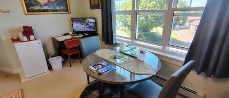 Un espacio habitable compacto con una mesa de comedor, sillas, un refrigerador pequeño, un televisor y una ventana con cortinas.