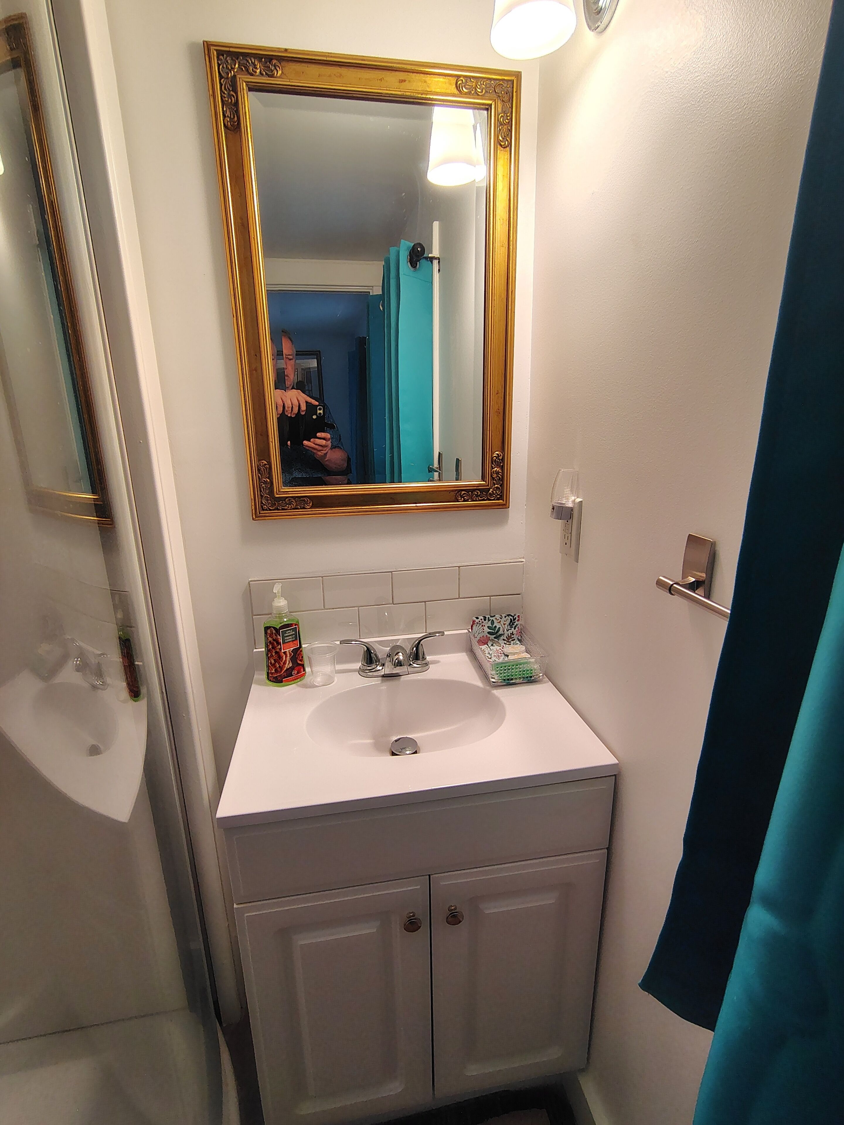 A bathroom with a white sink, a gold-framed mirror, and a blue shower curtain.