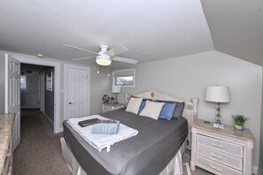 Un dormitorio con cama, mesitas de noche, ventilador de techo, ventana y puerta.