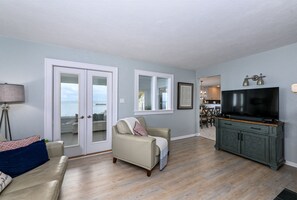 A living room with a sofa, a television, and a cabinet. There is a door leading to a balcony. - Waterfront Lake House with stunning views of Lake Erie! (Huron)