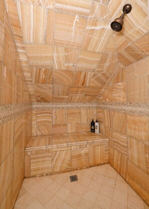 Un baño con suelo y paredes de mármol, un cabezal de ducha y dos botellas en el suelo.