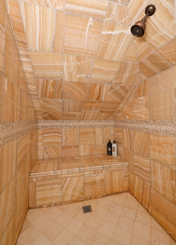 A bathroom with a marble floor and walls, a showerhead, and two bottles on the floor.