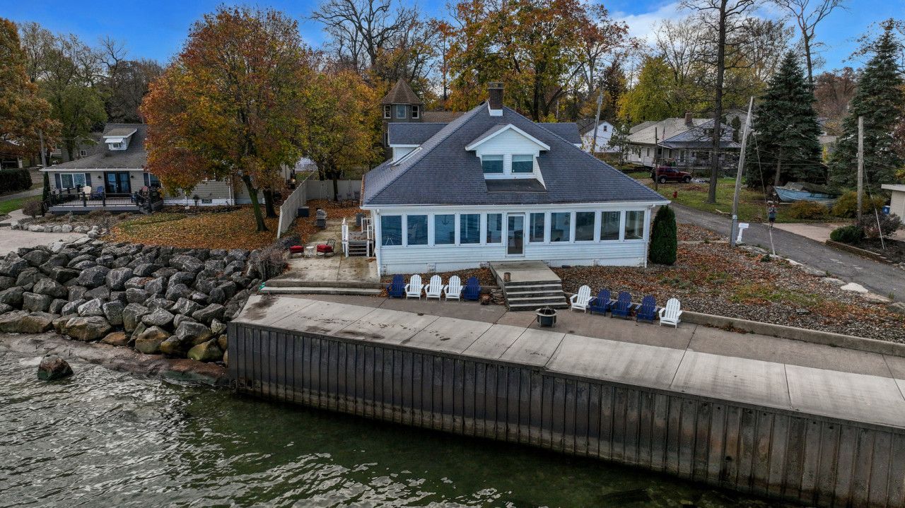 A docked house with a large windowed front, a stone wall, and a dock extending into a body of water.