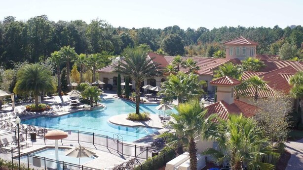 Een resort met een zwembad in het midden, palmbomen en een gebouw met een rode dakbedekking.