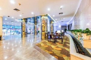 Um hall de hotel com piso de mármore, balcão de recepção e área de estar com cadeiras e mesas.