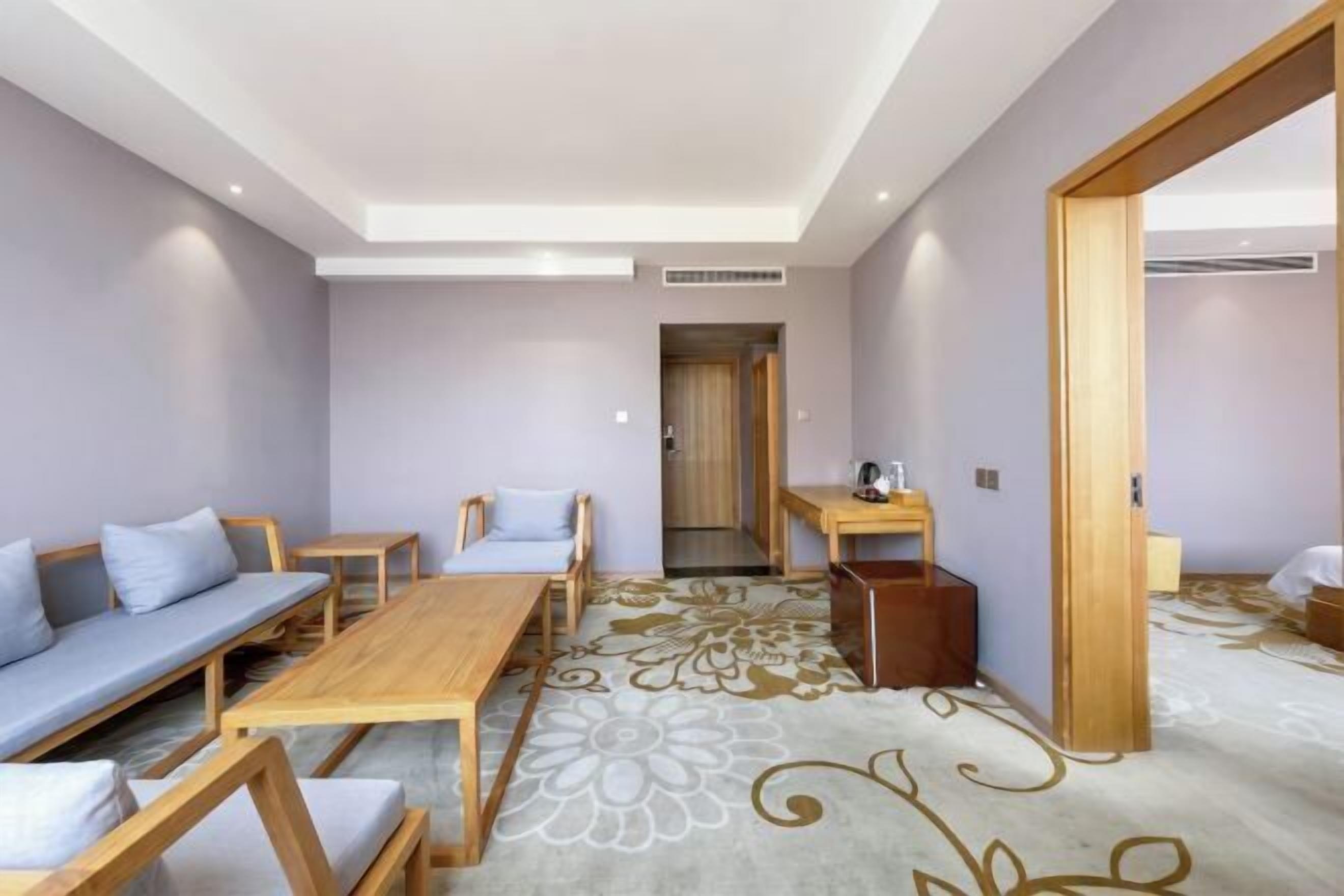 A modern hotel room with a sofa, a wooden table, and a small desk.