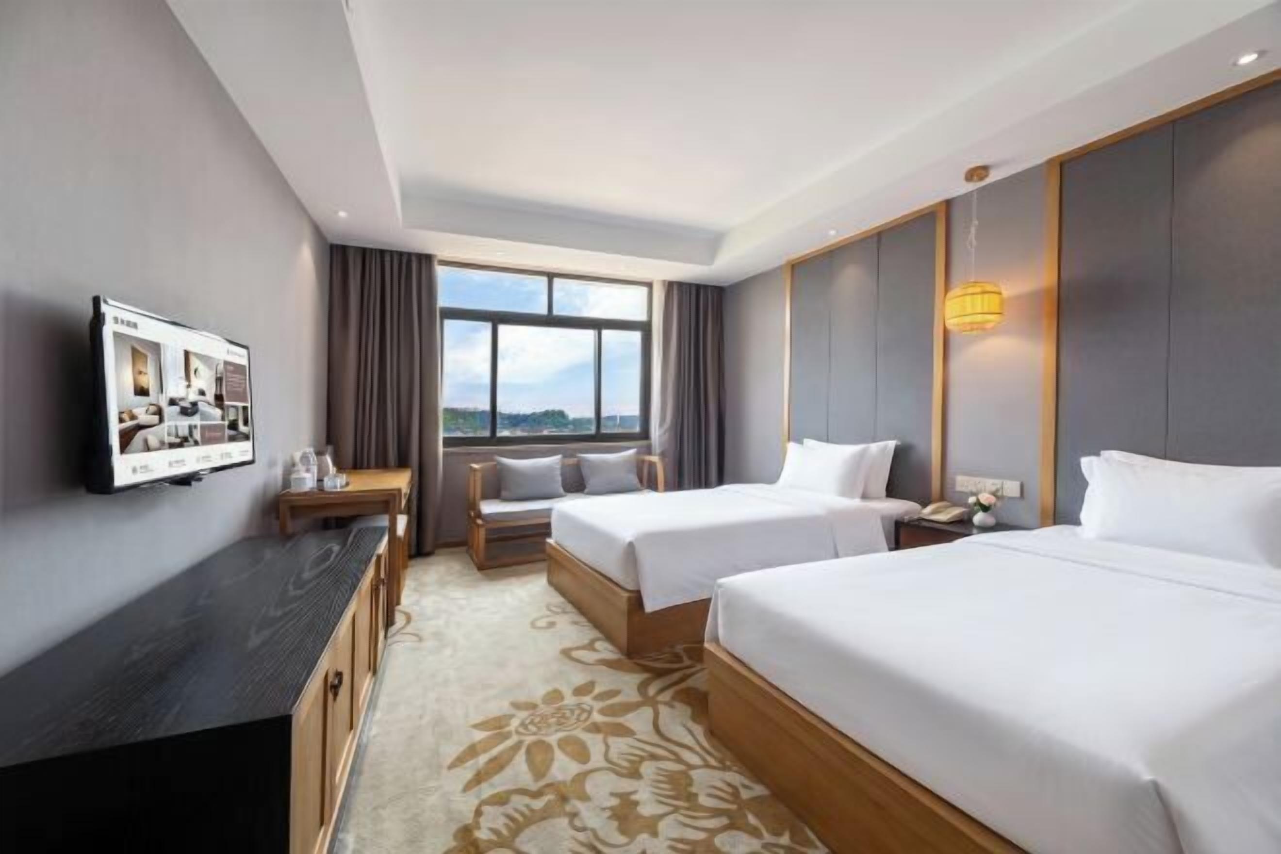 A hotel room with two beds, a TV, a desk, and a window with a view.