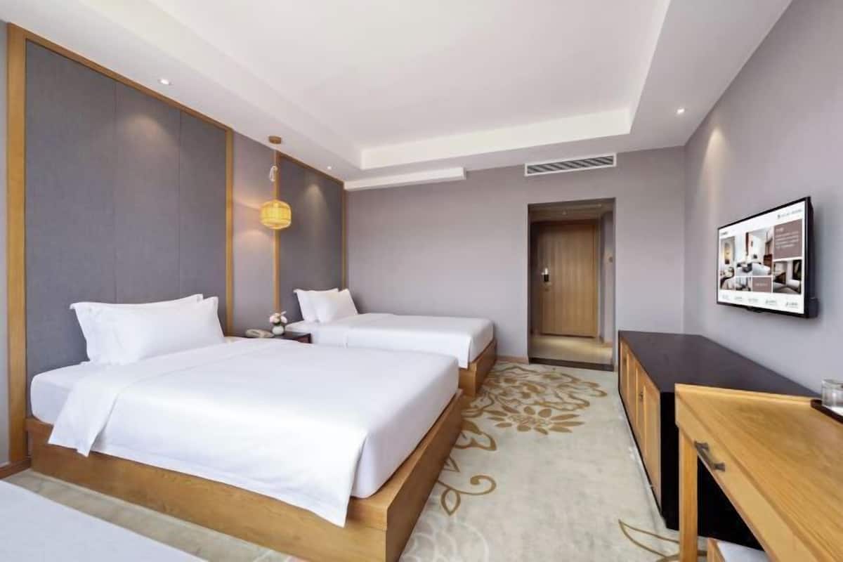 A hotel room with a large bed, bedside tables, a desk, and a door leading to another room.