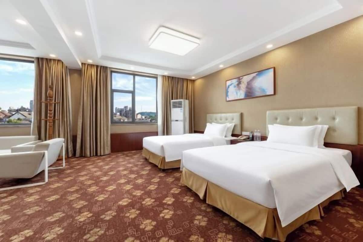 A hotel room with two beds, a sofa, a desk, and a window with a city view.