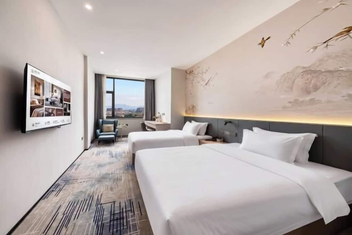 A hotel room with two beds, a desk, a chair, a TV, and a large window.