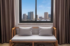 A wooden bench with two pillows, a window with a cityscape view, and brown curtains. - Lanjiang Hotel (Lanxi)