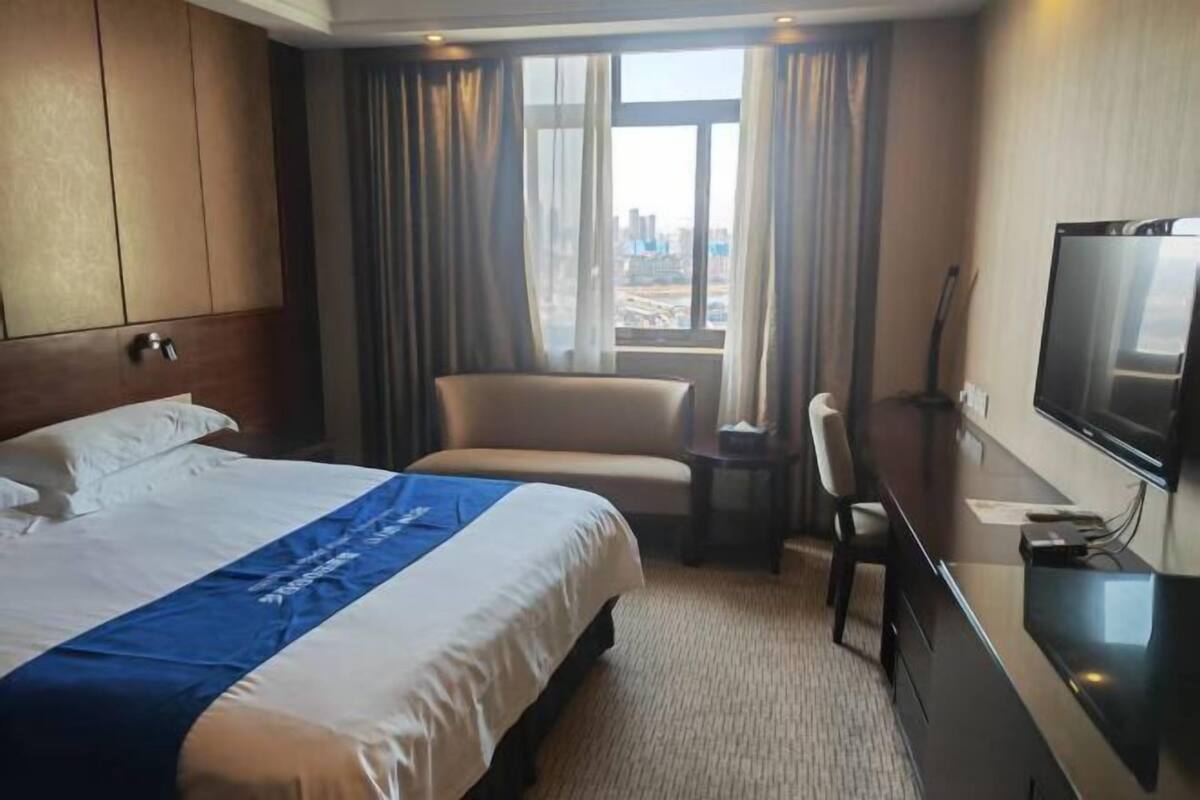 A hotel room with a bed, a desk, a chair, a television, and a window with curtains.