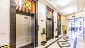 Et moderne elevatormiljø med tre elevatorer, hver med træpaneler og et mønstret gulv.