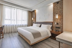 A hotel room with a large bed, a desk, a chair, a nightstand, and a wall-mounted light fixture. - Lanjiang Hotel (Lanxi)