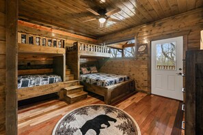 Una cabaña con literas, piso de madera, ventilador de techo y una puerta con ventanal.
