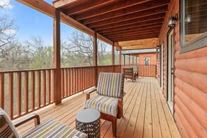 Una terraza de madera con dos sillas a rayas y una pequeña mesa, con vistas a una cabaña con ventana y puerta.