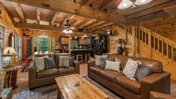 A wooden cabin interior with a sofa set, a dining table, and a kitchen area. - Cabin for 12 | 10 mins to Pkwy w/ Hot Tub & Games! (Sevierville)