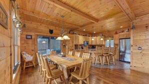 Interno di una baita in legno con tavolo da pranzo, sedie, angolo cottura e camino.