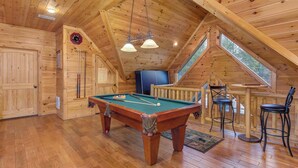 Un interno in legno con tavolo da biliardo, sedie, una sveglia e una finestra.