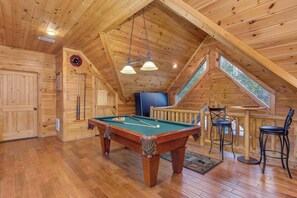 A wooden interior with a pool table, chairs, a clock, and a window.