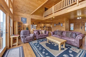 A log cabin interior with a balcony, wooden furniture, and a large rug. - Cabin w/ Mountain Views, Hot Tub & Game Room! (Sevierville)