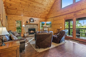 A log cabin interior with a fireplace, leather furniture, and a view through the glass door. - Rustic 3br Cabin Near Lake w/ Hot Tub! (Sevierville)