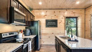 A modern kitchen with wooden walls, stainless steel appliances, and a granite countertop. - Modern Cabin w/ Pool, Hot Tub, Games & More! (Sevierville)