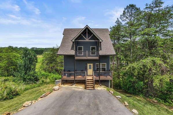 A two-story house with a balcony, surrounded by greenery. - Modern Cabin w/ Pool, Hot Tub, Games & More! (Sevierville)