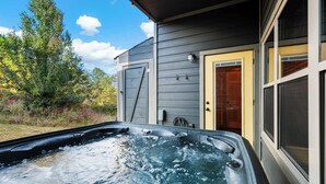 A hot tub outside a house with a wooden door and a window. - Modern Cabin w/ Pool, Hot Tub, Games & More! (Sevierville)