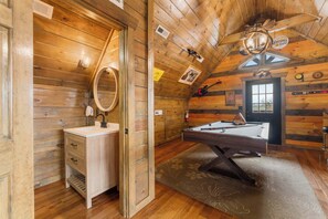 A wooden cabin interior with a wooden vanity, a pool table, and a ceiling fan.