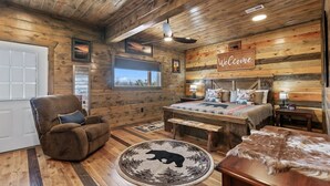 Une chambre confortable, aménagée dans le style d’un chalet, avec un lit, une chaise, un tapis rond et une table en bois.