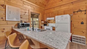 Une cuisine rustique aménagée dans une cabane en bois, avec un plan de travail en granit, deux chaises, un réfrigérateur et un four à micro-ondes.
