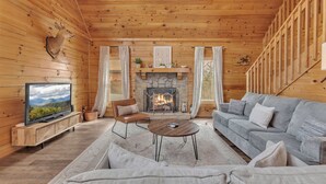 L’intérieur d’une cabane en rondins, avec une cheminée en pierre, une tête de cerf empaillée, un téléviseur, un canapé et un fauteuil.