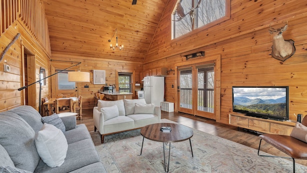 L’intérieur d’une cabane comprenant un canapé, une table basse, un téléviseur et une tête de cerf fixée au mur.