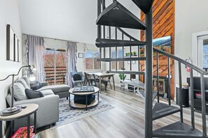 Uma sala de estar moderna com uma escada em espiral, um sofá, uma mesa de centro e uma lareira.