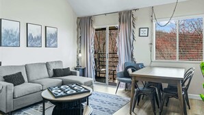 A living room with a sofa, coffee table, dining table, chairs, and a bookshelf.