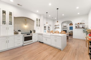 Cocina moderna con armarios blancos, una isla central e iluminación colgante.