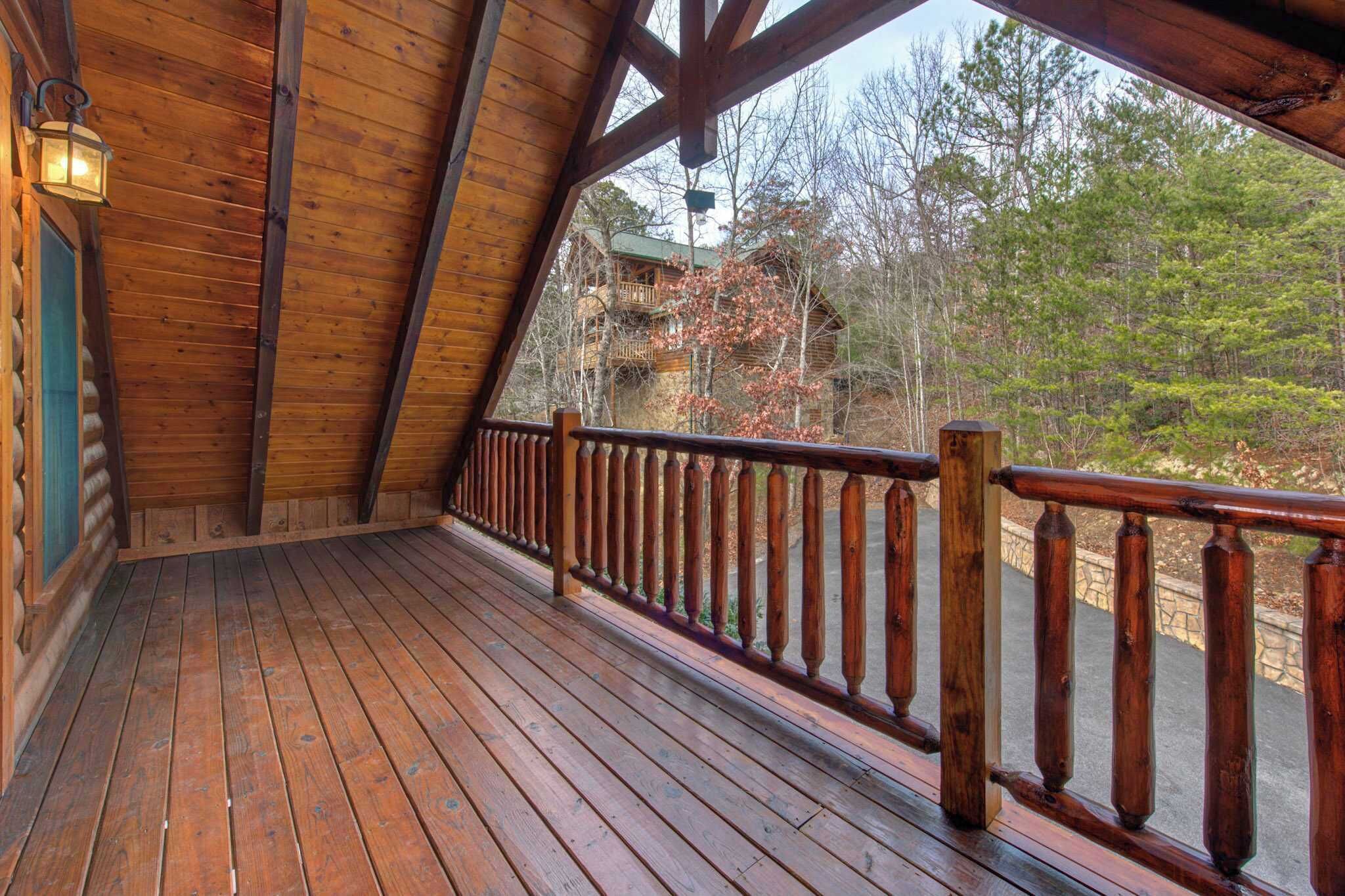 Une terrasse en bois avec une rambarde, une lanterne et une vue sur un chalet situé dans une forêt.