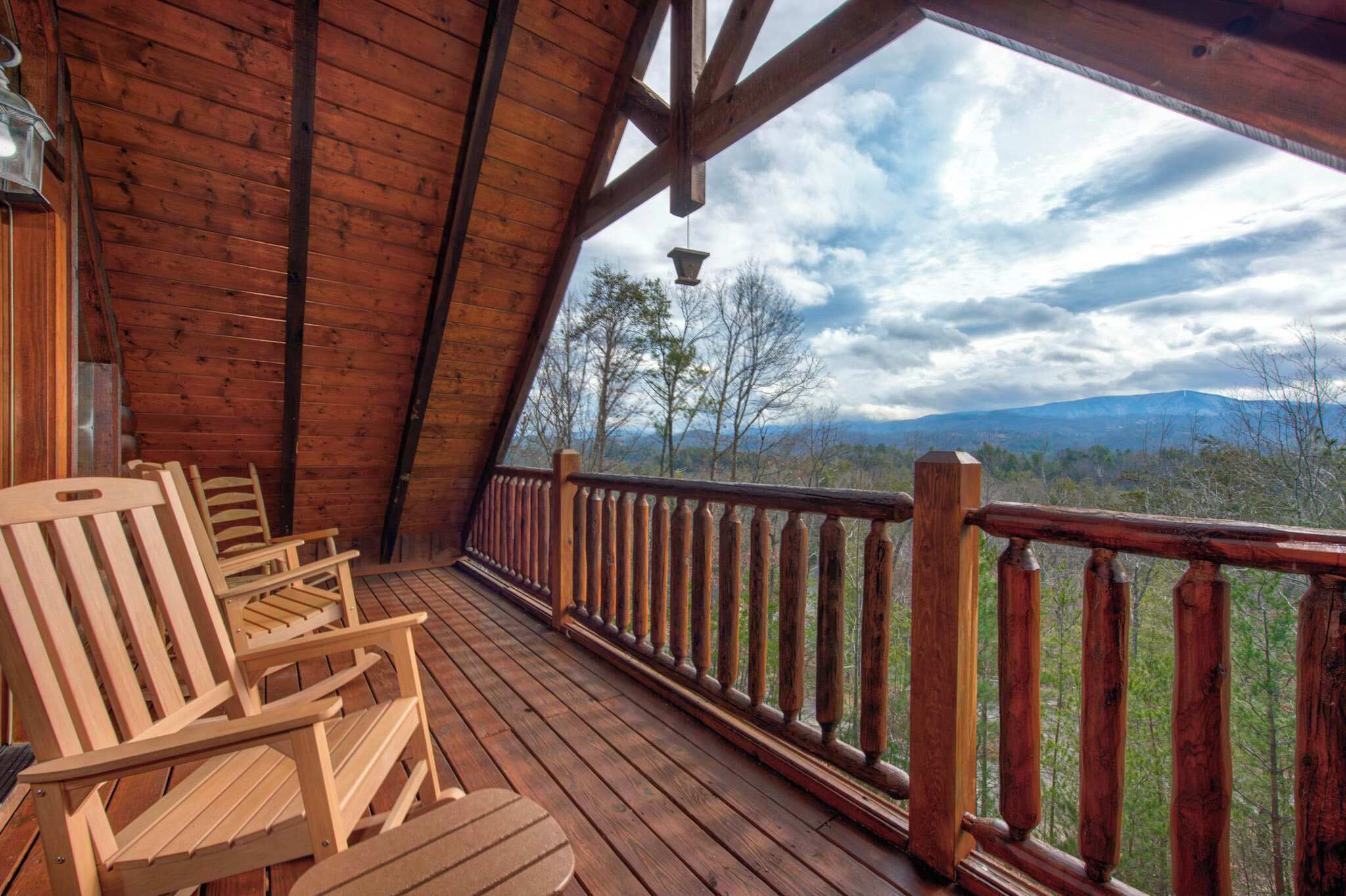 Une terrasse en bois, dotée de chaises Adirondack et d’une balustrade offrant une vue sur un paysage montagneux.