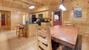 A wooden cabin interior with a kitchen, dining area, and a red door.
