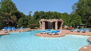 A swimming pool with blue lounge chairs, a waterfall feature, and a natural backdrop.