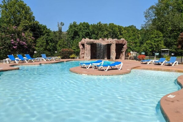 Ein Swimmingpool mit blauen Liegestühlen, einer Wasserfallanlage und einer natürlichen Kulisse.