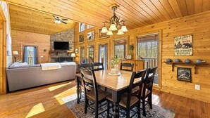 A wooden cabin interior with a dining area, a sofa, and a fireplace. - Woodland Wonder w/ Hot Tub & Pool Table! Sleeps 8! (Sevierville)