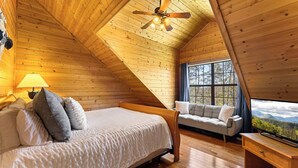 A cozy bedroom with a bed, a sofa, a TV, and a window with a view. - Woodland Wonder w/ Hot Tub & Pool Table! Sleeps 8! (Sevierville)