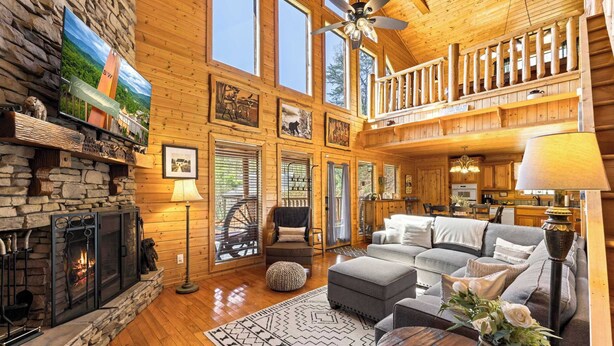 A spacious cabin with a stone fireplace, wooden walls, a balcony, and a cozy living area with a couch and ottoman. - Woodland Wonder w/ Hot Tub & Pool Table! Sleeps 8! (Sevierville)