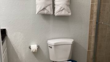 Een badkamer met toilet, twee handdoeken aan de muur, een lijst met afbeelding en een douchehoek.
